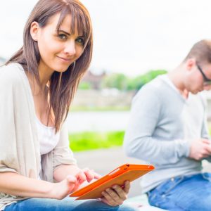 Woman sitting outside reading tablet device