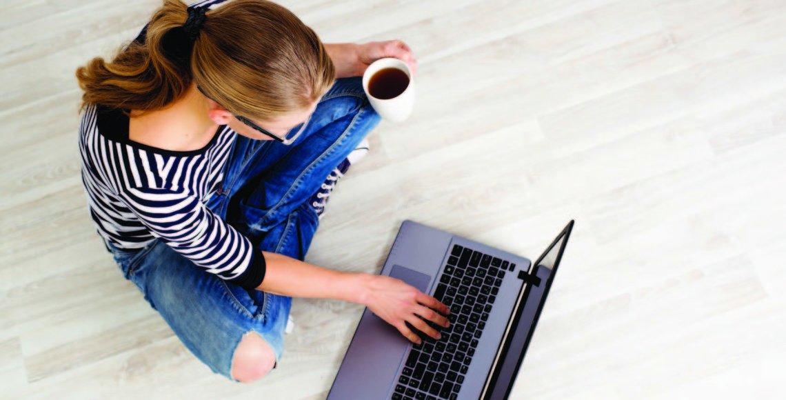 Woman sitting on floor working on computer with coffee in hand