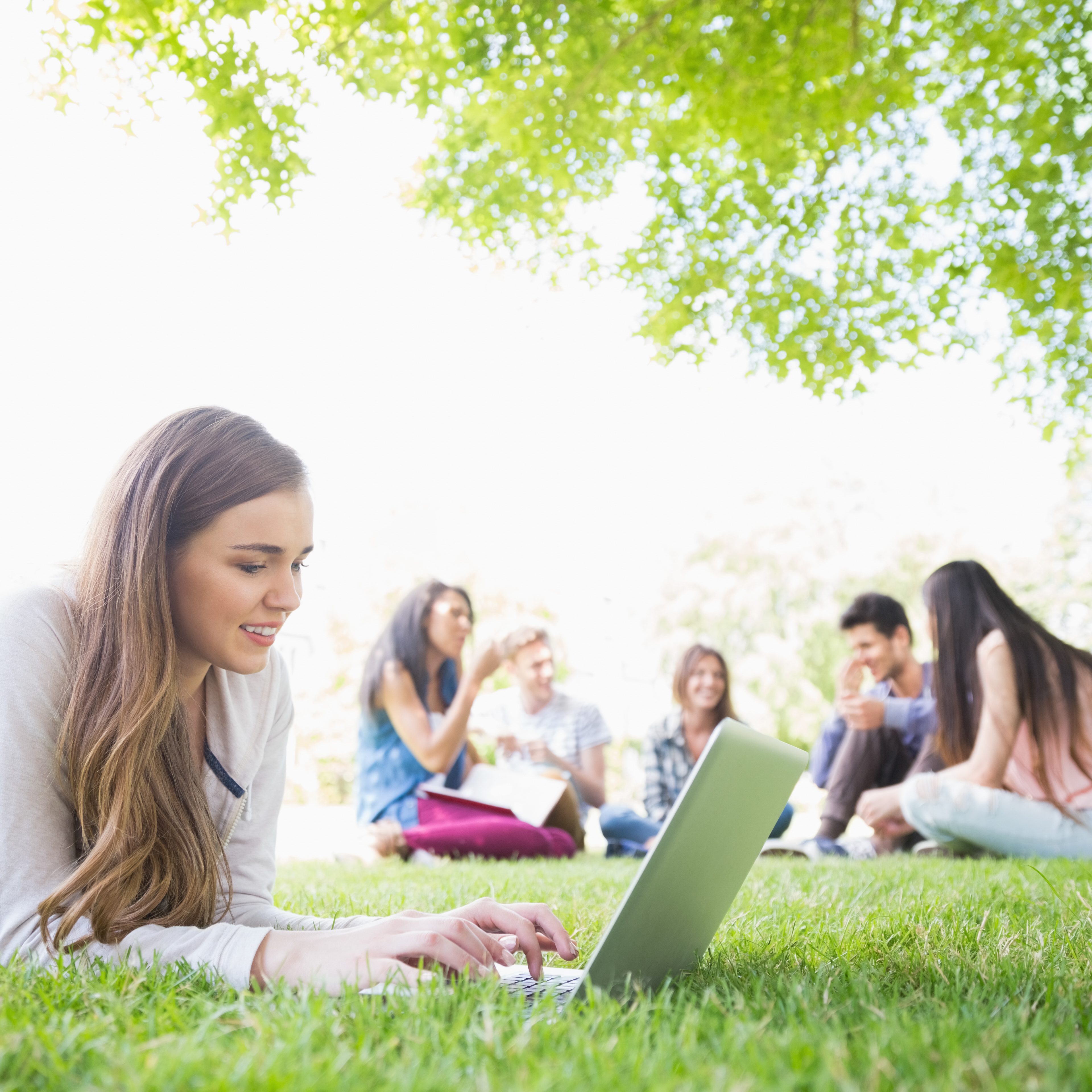 Using CDPs in higher education helps schools engage and attract students like these, sitting on a grassy lawn happily doing schoolwork